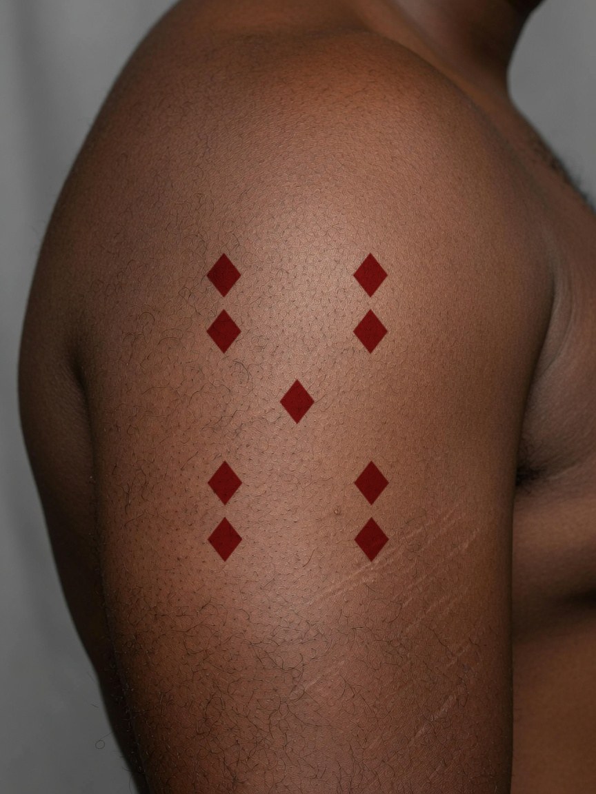 9 of Diamonds pip tattoo on the upper arm